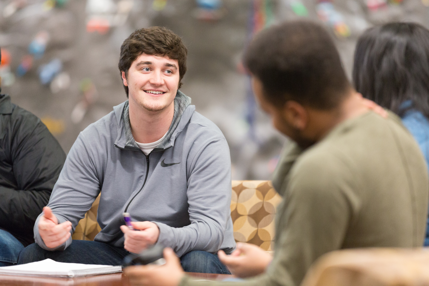 Student with brown short hair and grey nike zip up jacket on conversing with other students