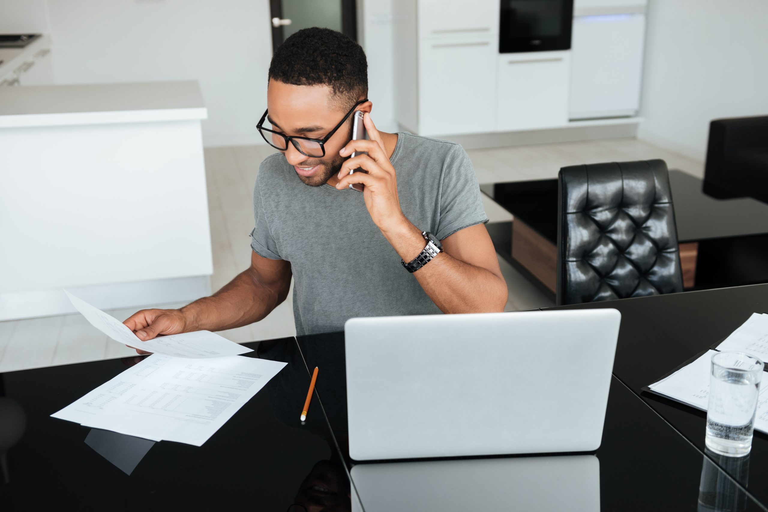 Man on the phone looking at paper at a desk.