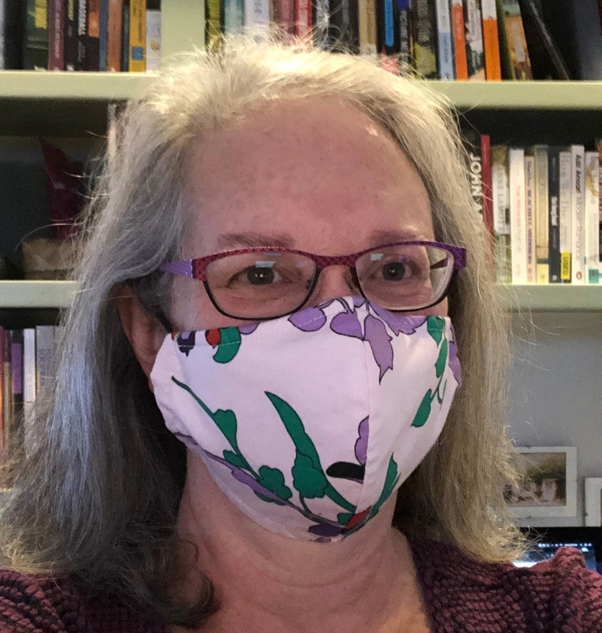 Sue Monahan wearing a non-surgical mask in front of shelves of books