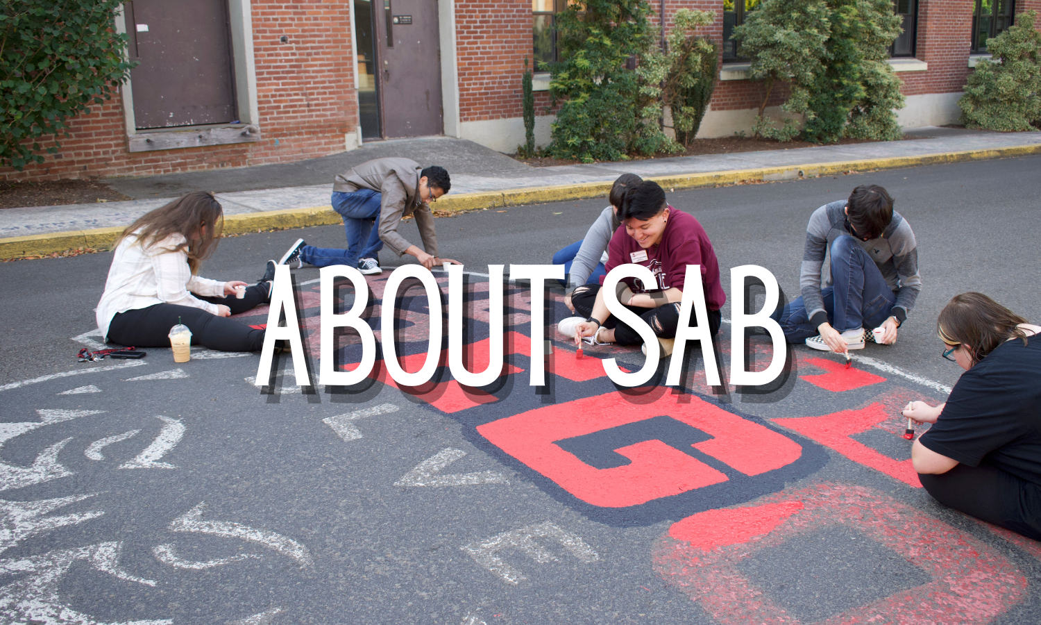 A group of students painting the WOU logo on the road. The words "About SAB" are superimposed over the students.