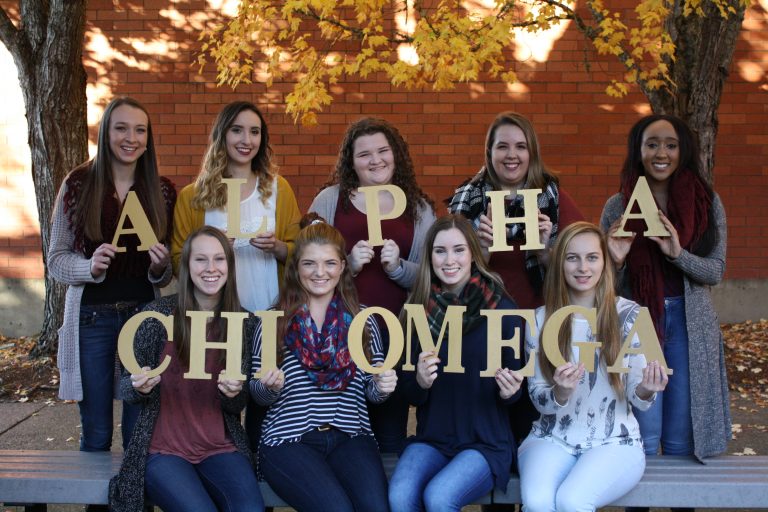 Alpha Chi Omega members posing in a group holding large wooden letters spelling out "Alpha Chi Omega."