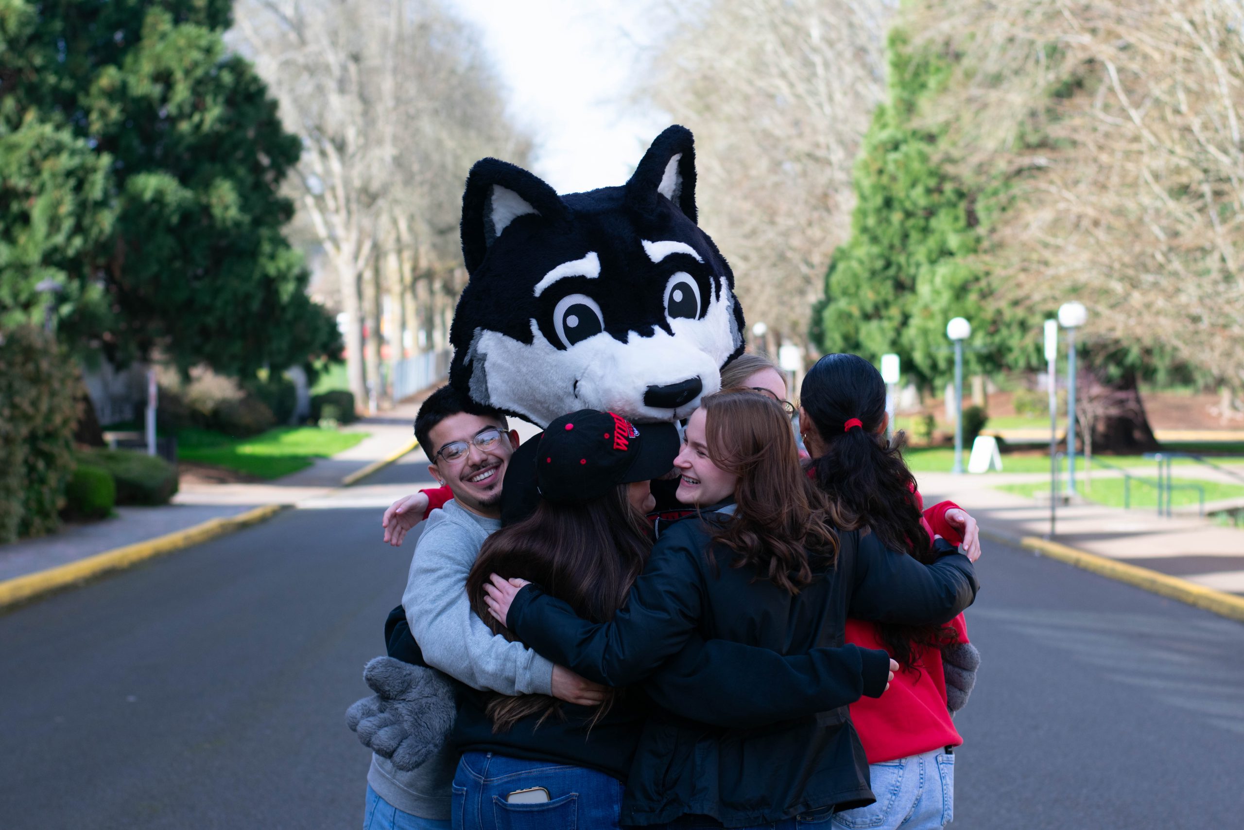Wolfie in a group hug with students. 