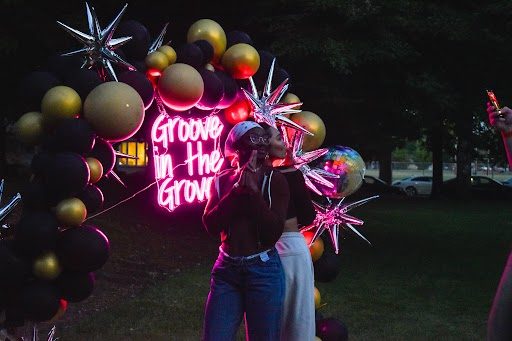 Two student posing in front of a neon Groove in the Grove sign. 