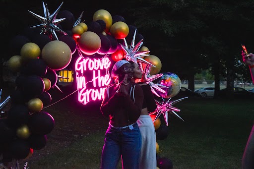 Two students posing in front of a neon sign that says Groove in the Grove.
